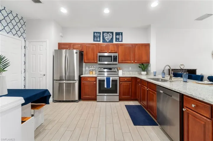 Kitchen with stainless steel appliances, light wood-type flooring, light stone countertops, and sink