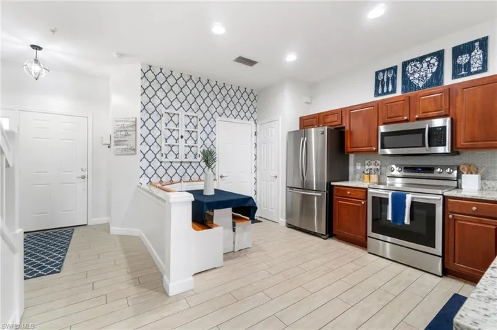Kitchen with stainless steel appliances, decorative light fixtures, light stone countertops, and backsplash