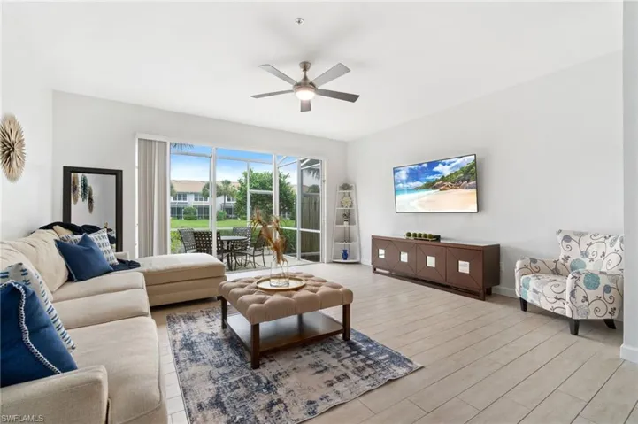 Living room featuring wood-like tile floors, fresh paint and ceiling fan and natural light from the sliding doors leading out to the screeded in lanai