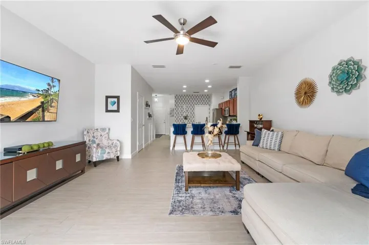 Living room with ceiling fan looking into the kitchen area with breakfast bar
