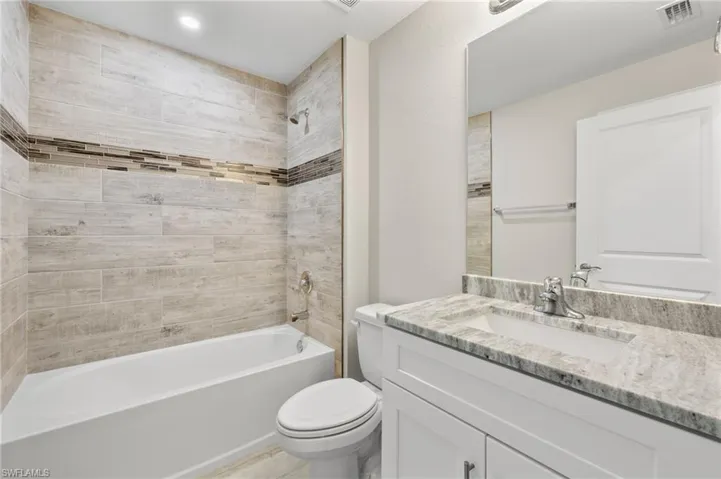 Full bathroom with vanity with extensive cabinet space, toilet, and tiled shower / bath