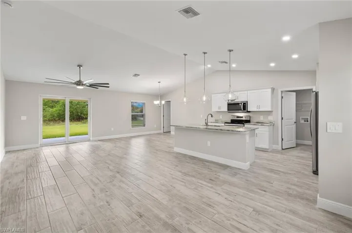 Kitchen featuring light hardwood / wood-style flooring, stainless steel appliances, a kitchen island with sink, white cabinets, and lofted ceiling