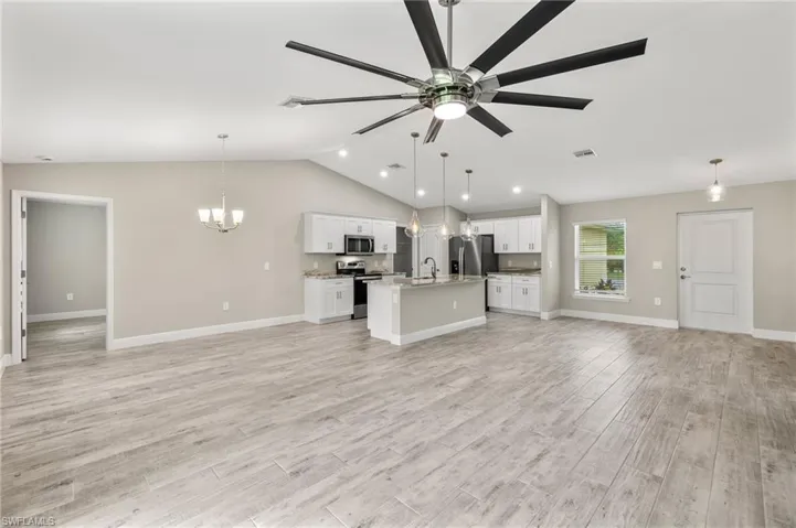 Unfurnished living room with ceiling fan with notable chandelier, sink, light hardwood / wood-style floors, and vaulted ceiling