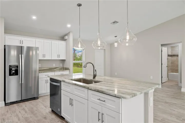 Kitchen with appliances with stainless steel finishes, white cabinetry, sink, and a center island with sink