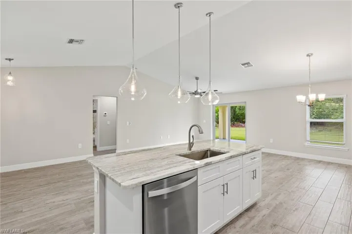 Kitchen with vaulted ceiling, light hardwood / wood-style floors, dishwasher, a center island with sink, and hanging light fixtures