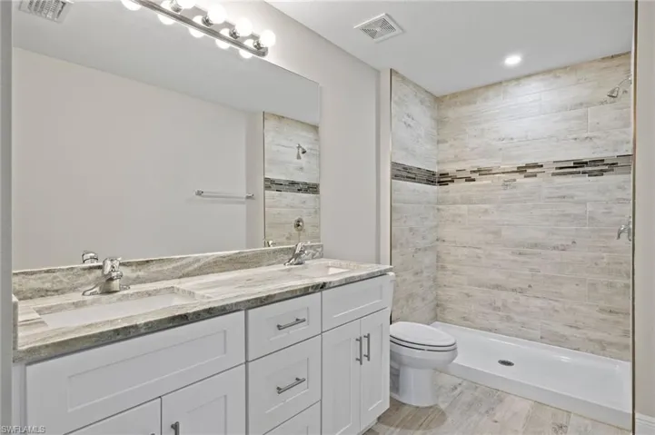 Bathroom featuring dual bowl vanity, hardwood / wood-style flooring, toilet, and a tile shower