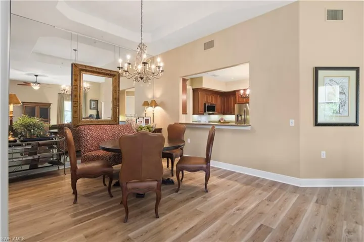 Dining space featuring light hardwood / wood-style floors, ceiling fan with notable chandelier, and a tray ceiling