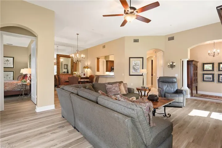 Living room featuring ceiling fan with notable chandelier, a raised ceiling, and light wood-type flooring