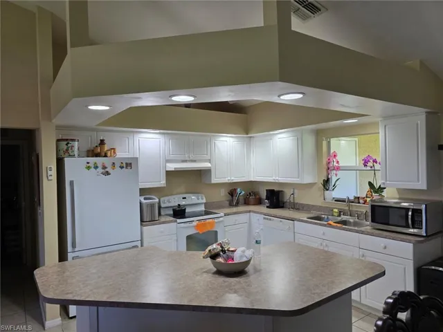 Kitchen with white cabinets, light tile patterned flooring, white appliances, a kitchen island, and under cabinet range hood