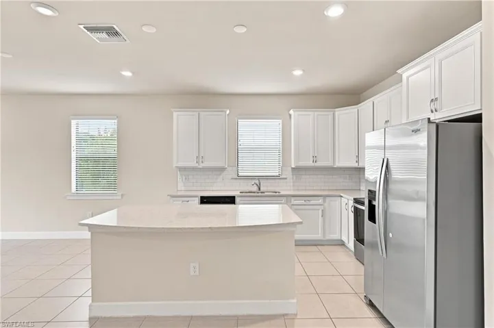 Kitchen featuring a large island with a light-toned countertop, white cabinetry, stainless steel appliances, and a subway tile backsplash