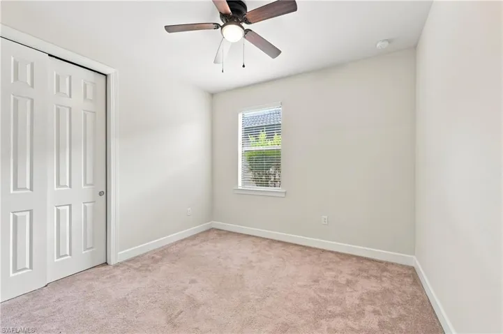 Bright bedroom featuring neutral carpeting, a ceiling fan with integrated lighting, a large window with plantation shutters, a six-panel closet door, and fresh white walls