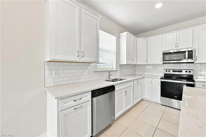 White cabinetry with silver hardware, subway tile backsplash, stainless steel appliances, dual basin sink, and tile flooring