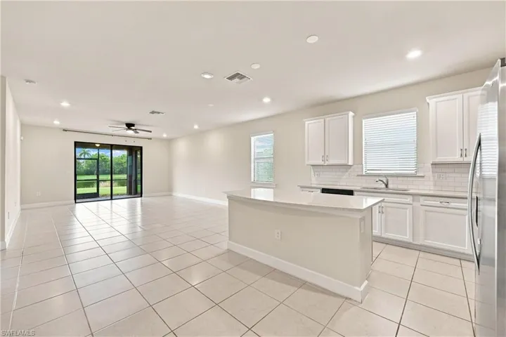 Bright and spacious open-concept kitchen and great room featuring white cabinetry with hardware accents, stainless steel appliances, tile flooring throughout, a large center island with seating, recessed lighting, and French doors opening to the exterior