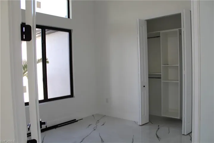 Unfurnished bedroom featuring multiple windows, light marble finish flooring, and a closet