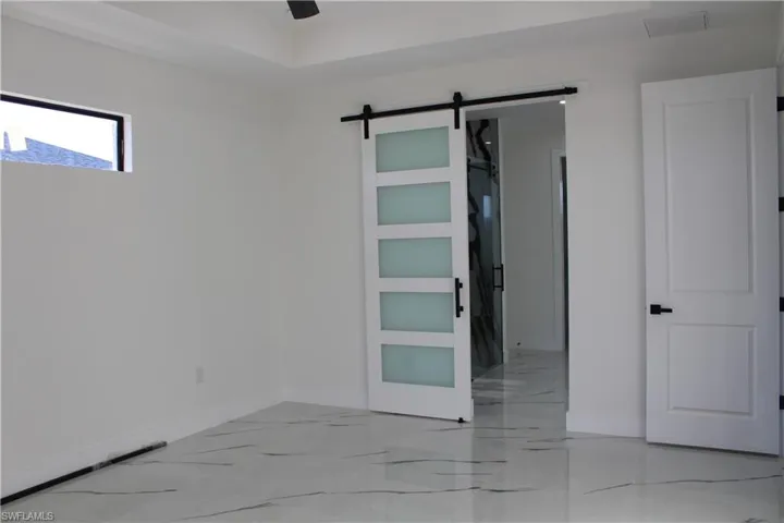 Unfurnished bedroom with a barn door, baseboards, and light marble finish flooring