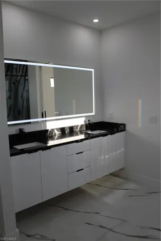 Bathroom with double vanity, baseboards, marble finish flooring, and recessed lighting