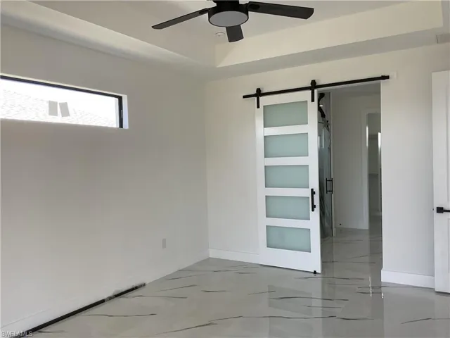 Empty room featuring marble finish floor, baseboards, a ceiling fan, and a barn door