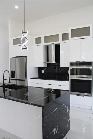 Kitchen with fridge, modern cabinets, multiple ovens, range hood, and white cabinetry