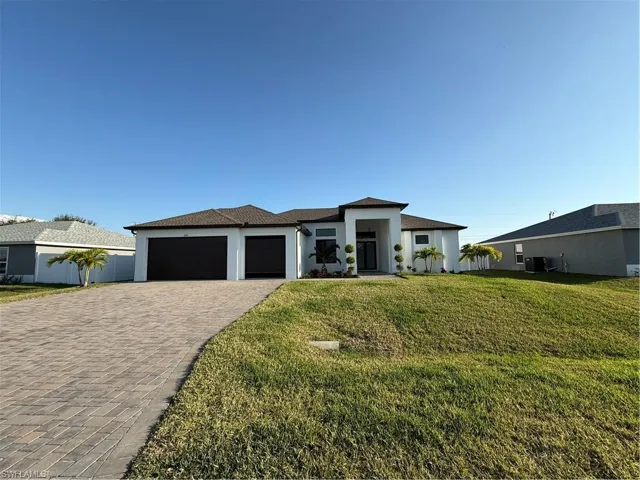 Prairie-style house featuring central AC, an attached garage, stucco siding, a front lawn, and decorative driveway