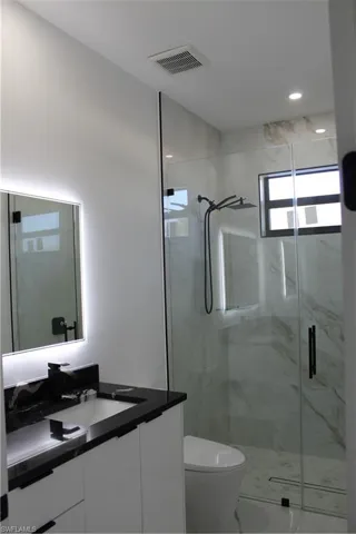 Bathroom with vanity, a marble finish shower, toilet, and marble look tile flooring