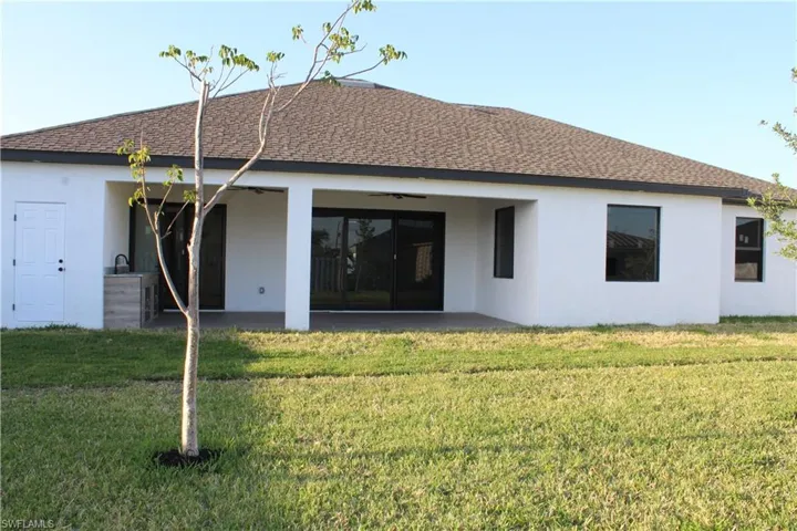 Back of property featuring stucco siding, a lawn, a patio, and roof with shingles