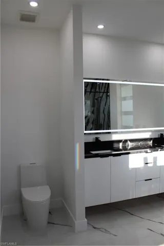 Bathroom featuring vanity, toilet, baseboards, recessed lighting, and marble finish floors