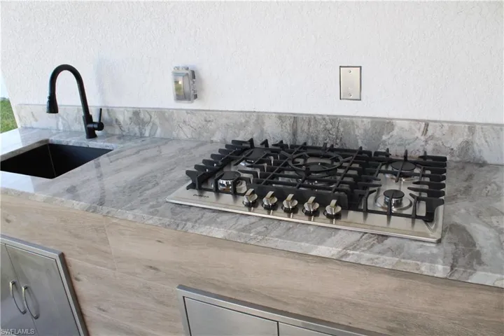 Kitchen view of a sink, stainless steel gas stovetop, and light stone countertops