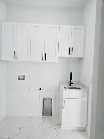 Utility room featuring a built-in sink with a matte black faucet, white shaker-style cabinetry with black hardware, and marble-look tile flooring