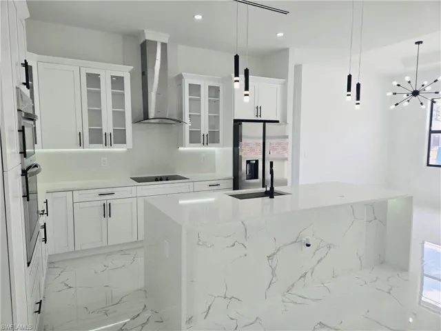White kitchen featuring a waterfall island, integrated sink with matte black faucet, stainless steel appliances, and under-cabinet lighting