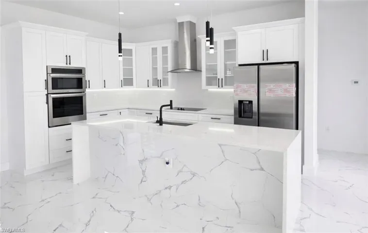 Modern kitchen featuring white cabinetry, stainless steel appliances, a large waterfall island with integrated sink, pendant lighting, and marble-look flooring