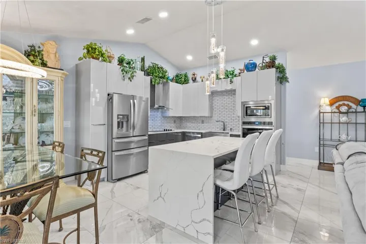 A true chef’s dream featuring a large breakfast island, high-gloss acrylic cabinetry, tiled backsplash, and designer finishes throughout.