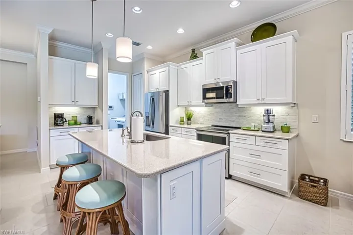 Kitchen with decorative backsplash, hanging light fixtures, white cabinets, light tile patterned floors, and stainless steel appliances