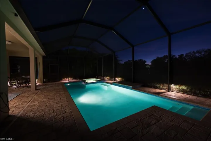 Pool at night featuring an in ground hot tub, a lanai, and a patio area