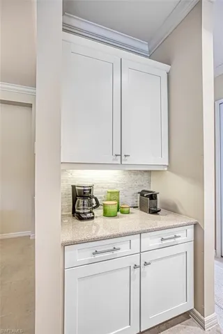 Bar with white cabinetry, crown molding, decorative backsplash, and light stone countertops