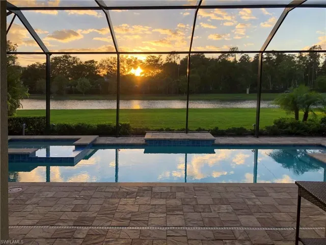 Pool at dusk with glass enclosure, a water view, and a yard