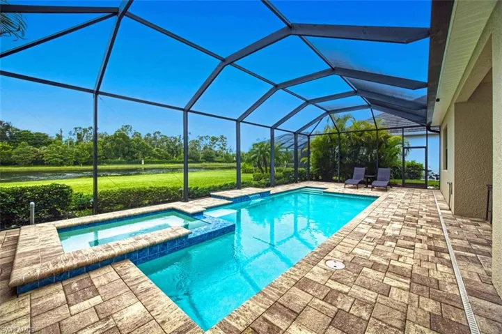 View of swimming pool with glass enclosure, an in ground hot tub, and a patio