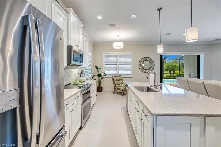 Kitchen with a kitchen island with sink, white cabinetry, light stone countertops, sink, and stainless steel appliances