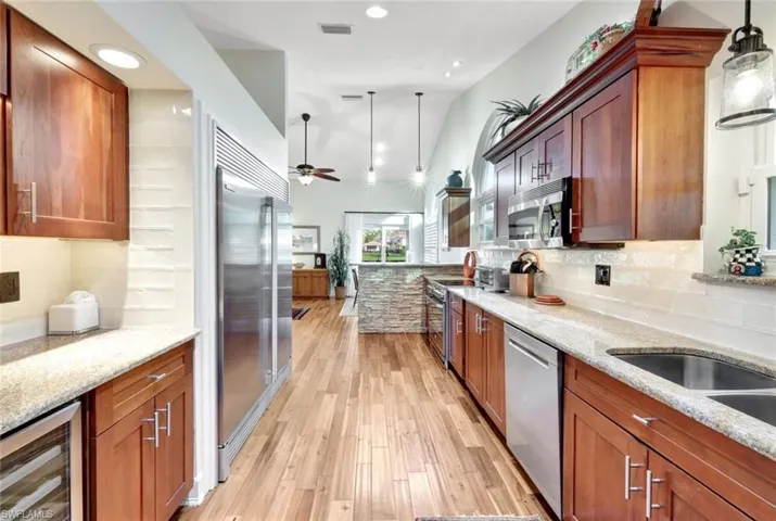 Kitchen with wine cooler, ceiling fan, appliances with stainless steel finishes, decorative light fixtures, and light stone counters