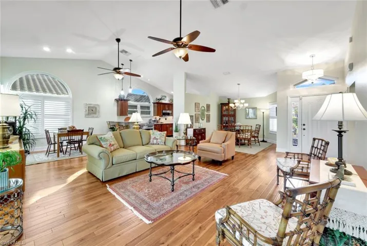 Living room with lofted ceiling, light hardwood / wood-style floors, and ceiling fan with notable chandelier