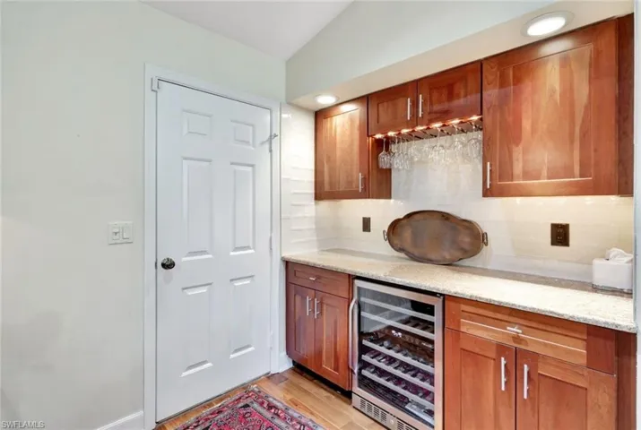 Bar featuring decorative backsplash, light stone counters, wine cooler, and vaulted ceiling