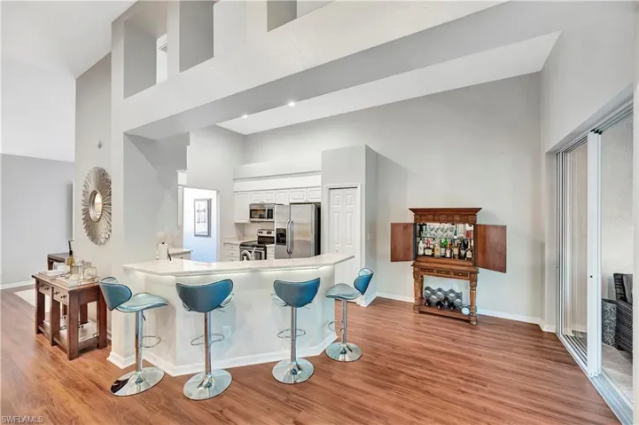 Kitchen with a breakfast bar, light wood-style flooring, a towering ceiling, appliances with stainless steel finishes, and white cabinetry