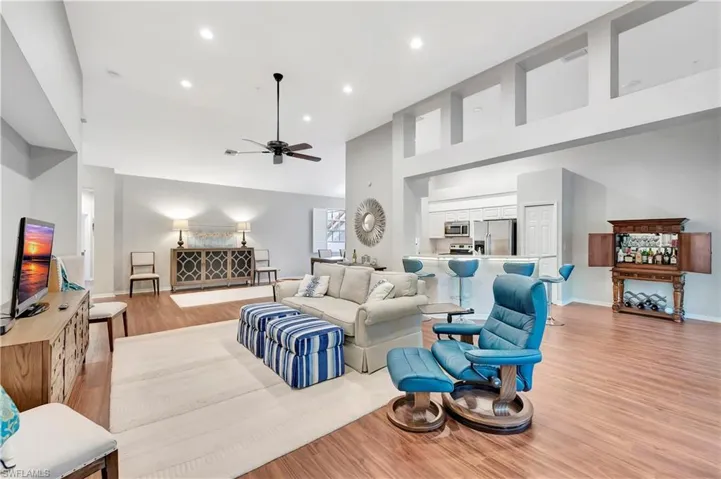 Living area featuring light wood-style flooring, a ceiling fan, recessed lighting, a high ceiling, and baseboards