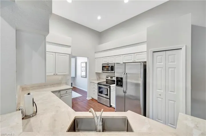 Kitchen with light stone counters, appliances with stainless steel finishes, wood finished floors, white cabinetry, and a sink