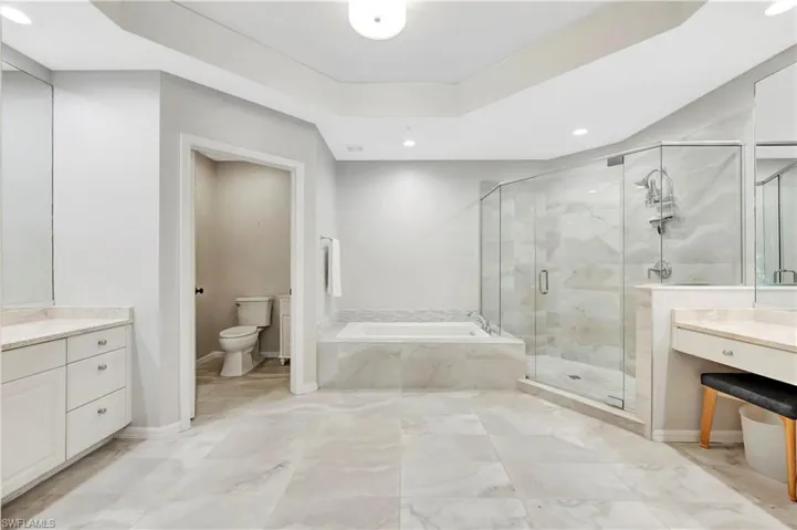 Bathroom with vanity, baseboards, a shower stall, a garden tub, and toilet