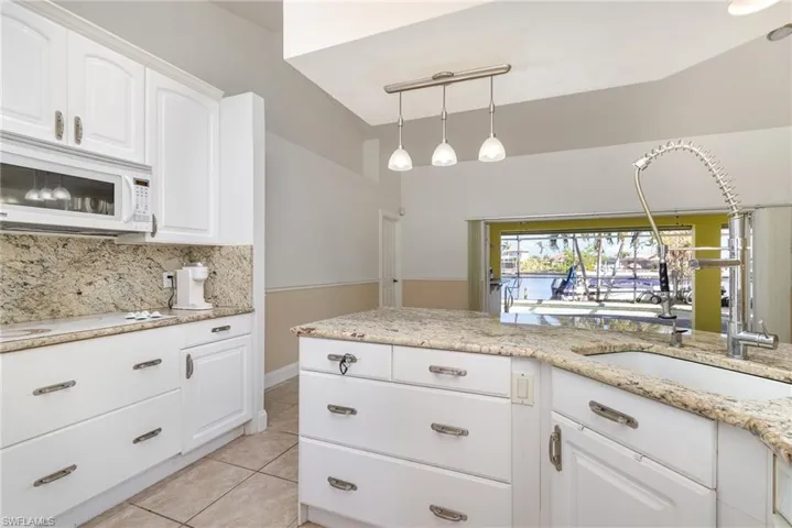 Kitchen with granite tops and backsplash, lofted ceiling, white cabinets, light tile patterned floors, tasteful backsplash, and decorative light fixtures