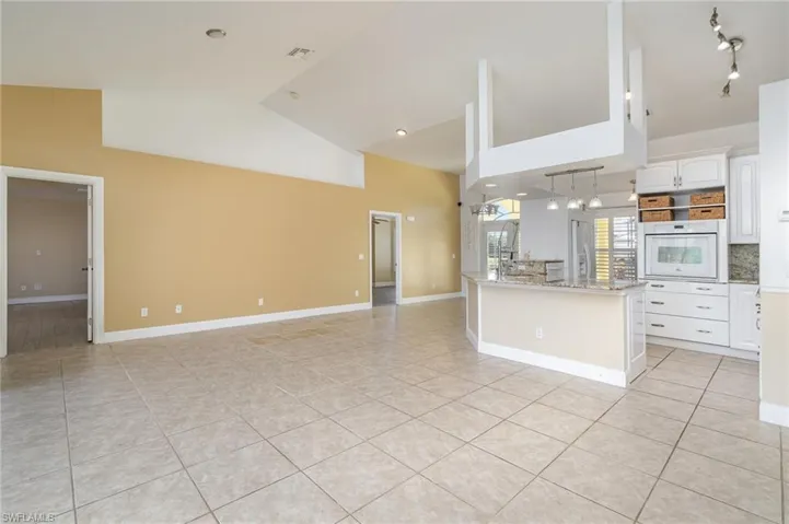 Kitchen featuring white oven, white cabinets, light tile patterned flooring, and high vaulted ceiling
