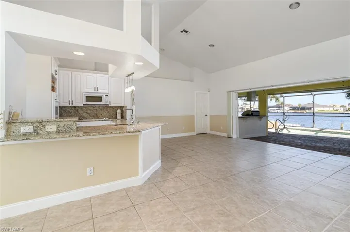 Kitchen with a water view, hanging light fixtures, white cabinetry, light stone counters, and kitchen peninsula