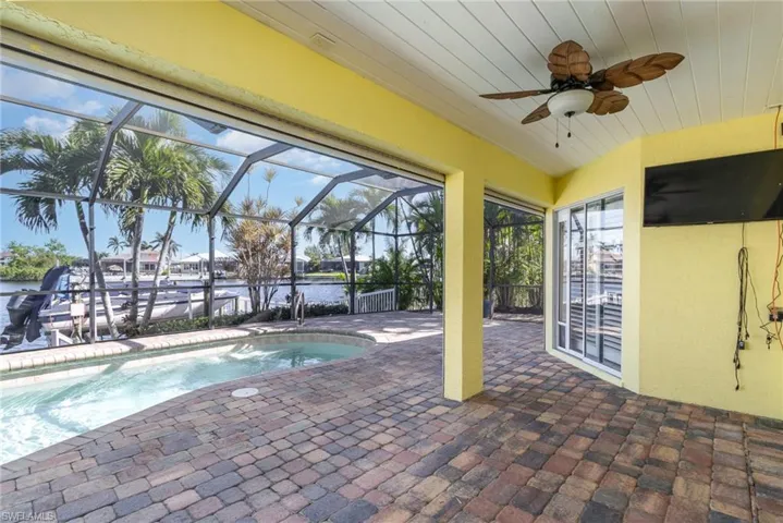 View of swimming pool featuring glass enclosure, ceiling fan, and a patio area