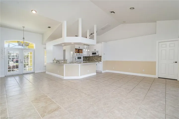Unfurnished living room with light tile patterned floors, french doors, high vaulted ceiling, and an inviting chandelier