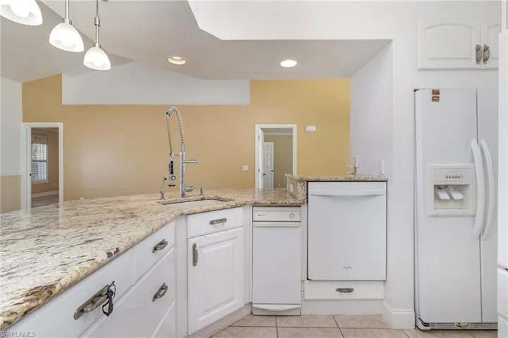 Kitchen featuring light stone countertops, white cabinets, pendant lighting, white appliances, and light tile patterned flooring